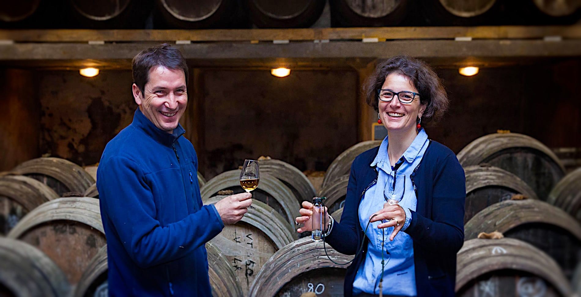 Line Sauvant et son mari devant leur tonneaux, chacun avec un verre à la main.